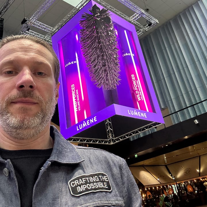 Santeri Salmi in front of one of his installations: a tall screen in a shopping centre showing a purple box that appears to hang out of the display.